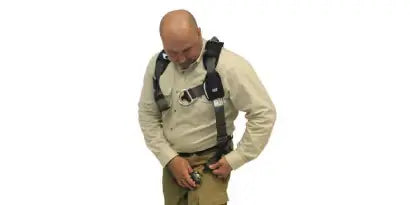 A worker, with the shoulder straps on, is shown bending over to securely fasten one of the leg straps using a quick-connect buckle. He is making sure the straps are positioned correctly to protect the upper legs and groin area.