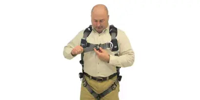 A worker is shown fastening and adjusting the front chest strap buckle to ensure a snug and centered fit across the sternum. He is also adjusting the harness waist belt, which should sit just above the hips.
