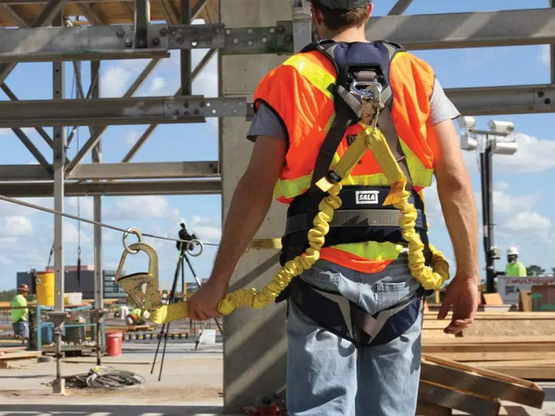 This image shows a worker on a construction site secured by a twin-leg, shock-absorbing safety lanyard attached to their harness. Lanyards come in positioning or shock-absorbing forms, controlling worker movement and limiting fall arrest forces.