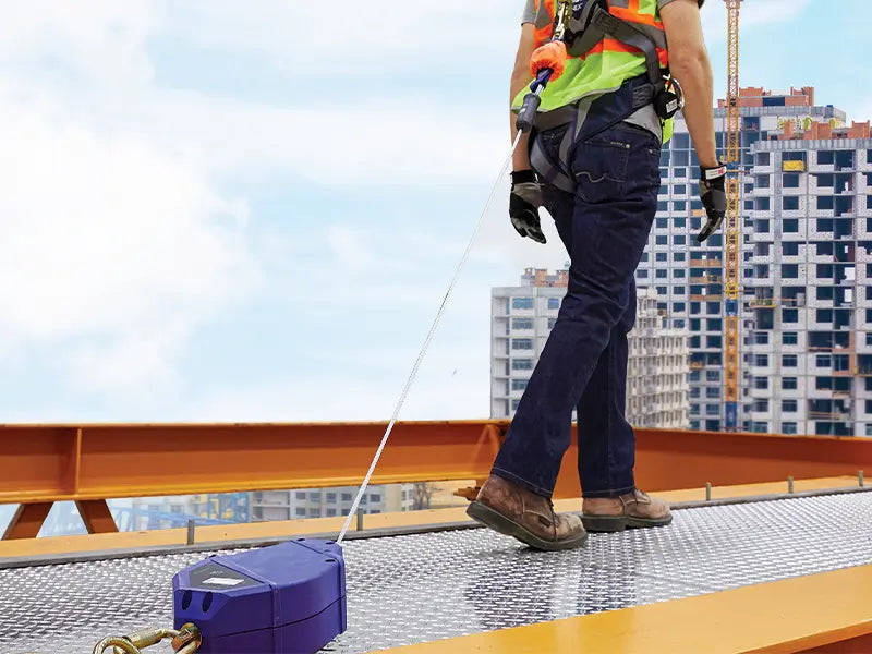 This image depicts a worker on a grated platform using a Self-Retracting Lifeline (SRL) unit to secure their movements. SRLs retain tension on the lifeline, which minimizes trip hazards, shortens the fall distance, and improves worker mobility.